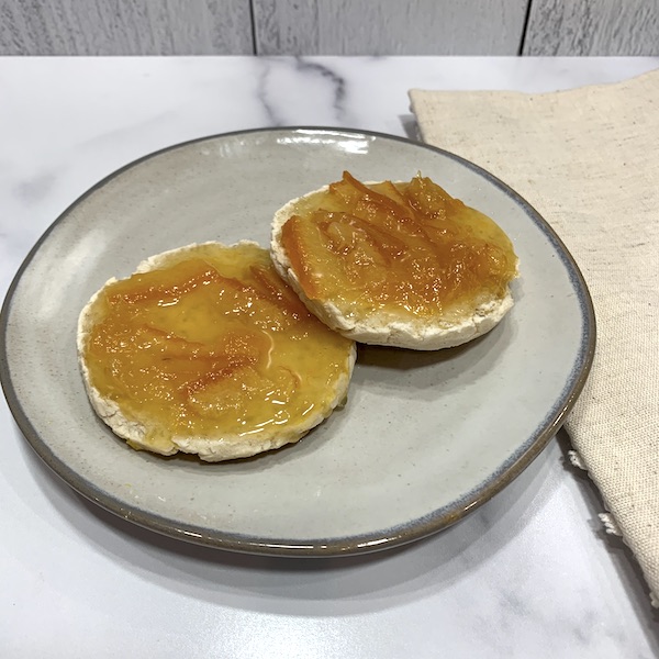 gluten free vegan English muffin split open on a grey plate and covered with homemade marmalade