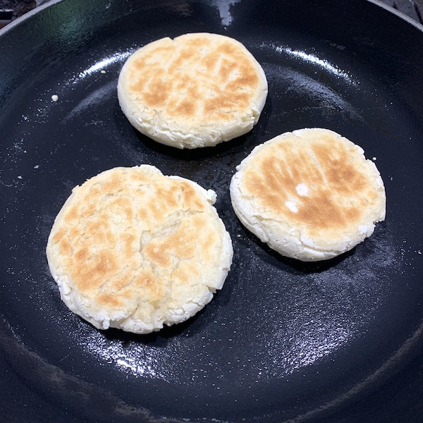 3 gluten free vegan english muffins cooking in a cast iron skillet on the stove