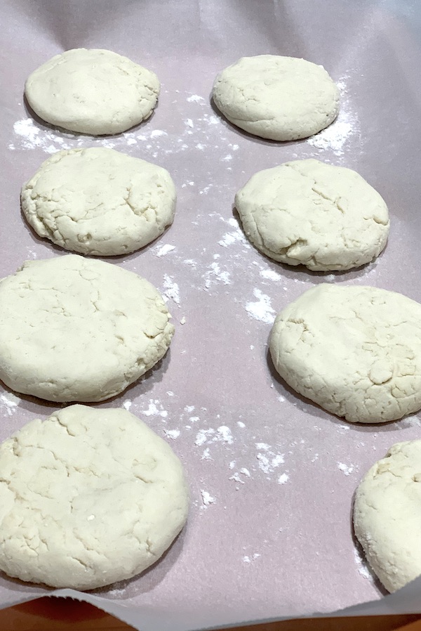 gluten free vegan english muffins on their second rise on a parchment lined pan